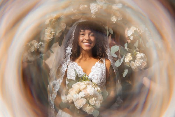 A bride wearing a white dress holds flowers while smiling at the camera.