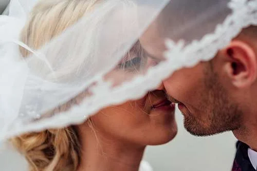 a bride and groom kissing underneath a veil