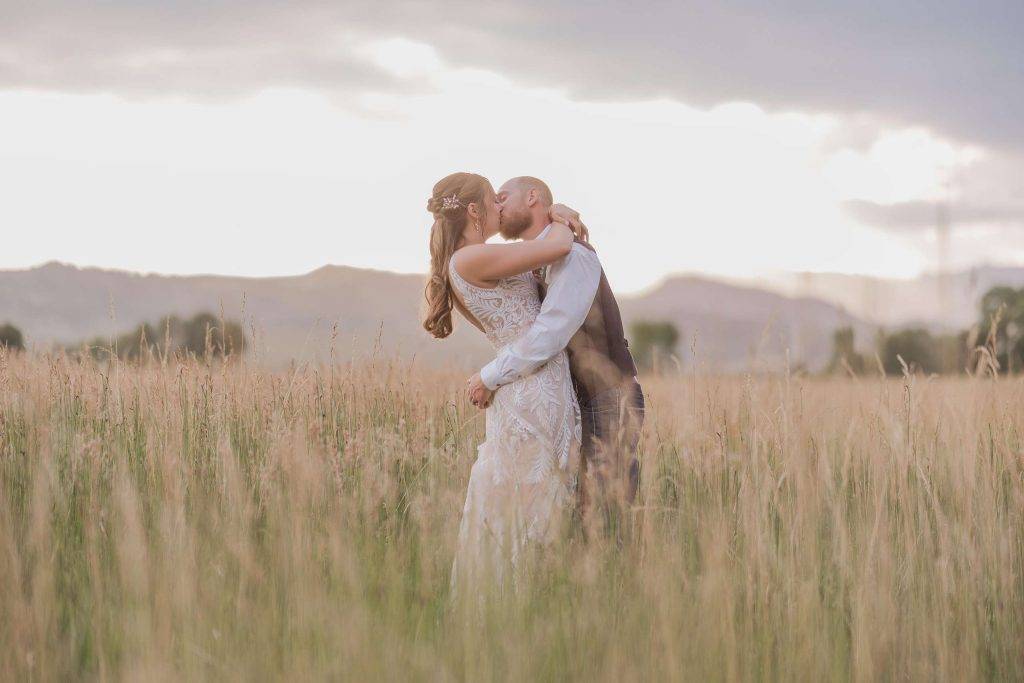 Bride and groom kissing in tall grasses of the Colorado foothills during their wedding at Shoupe Homestead wedding venue.