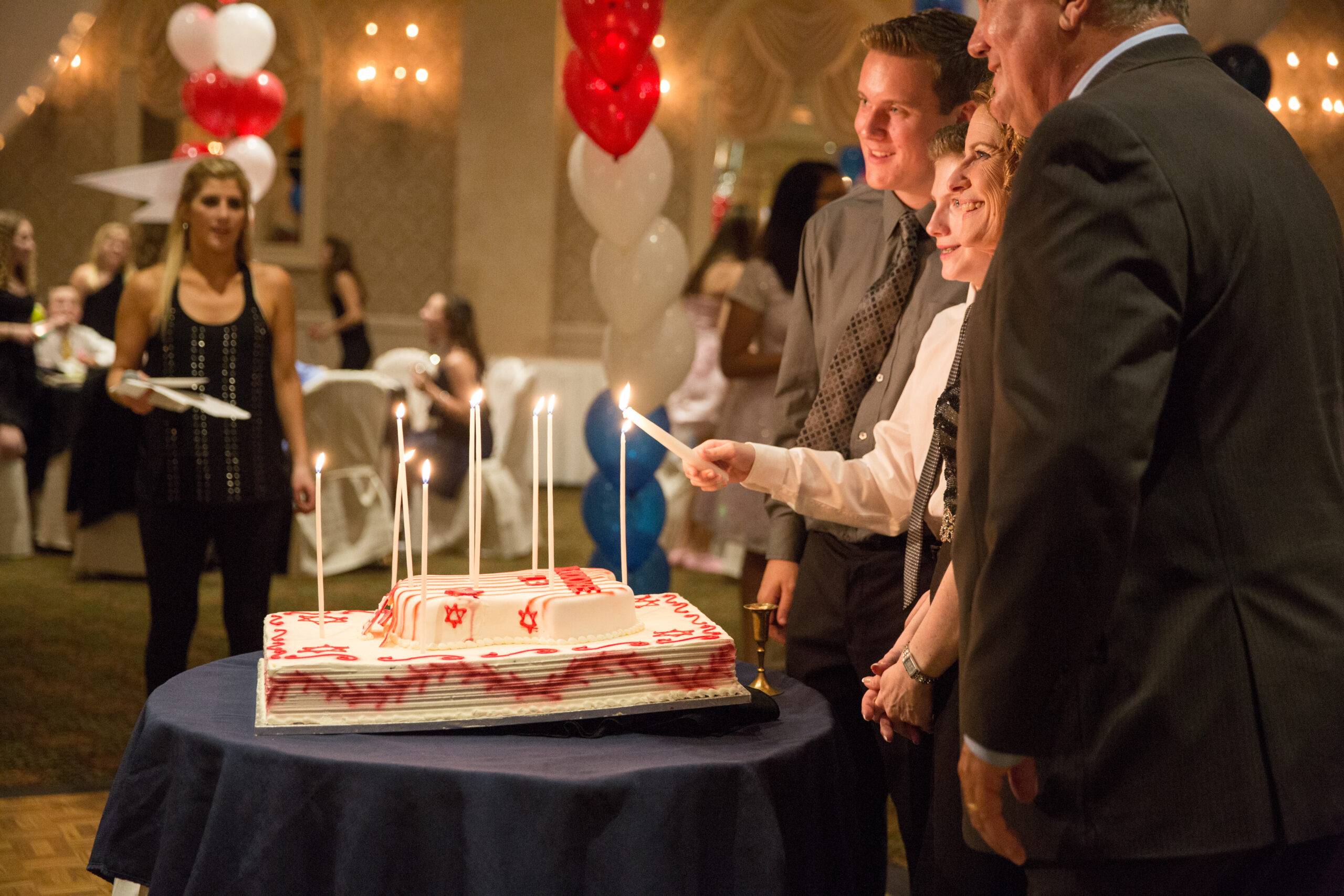 Bar Mitzvah boy lights candles on his cake with his family