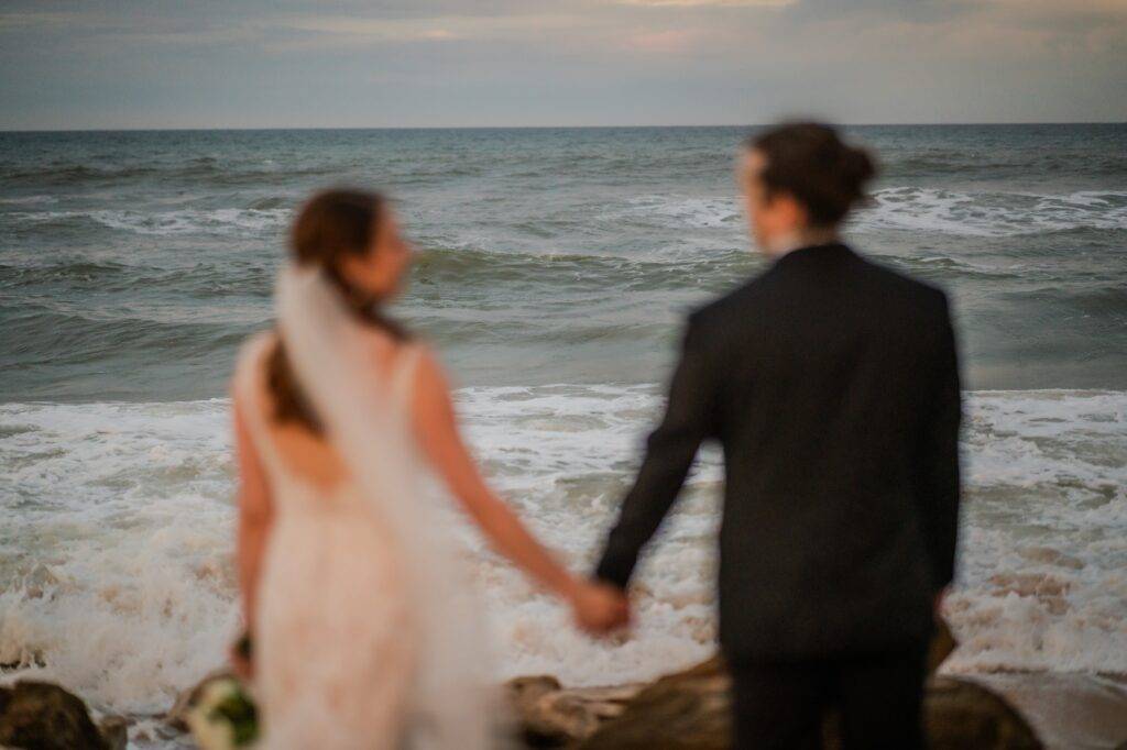Bride and groom holding hands looking out over the ocean.